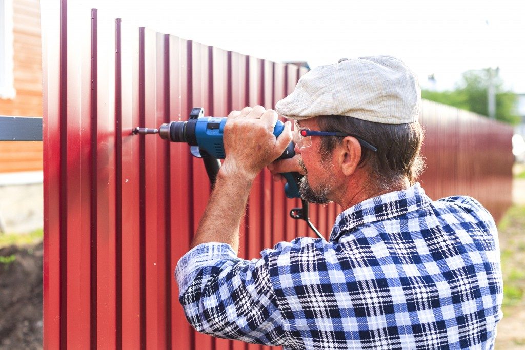 an elderly man with a drill builds metal fence